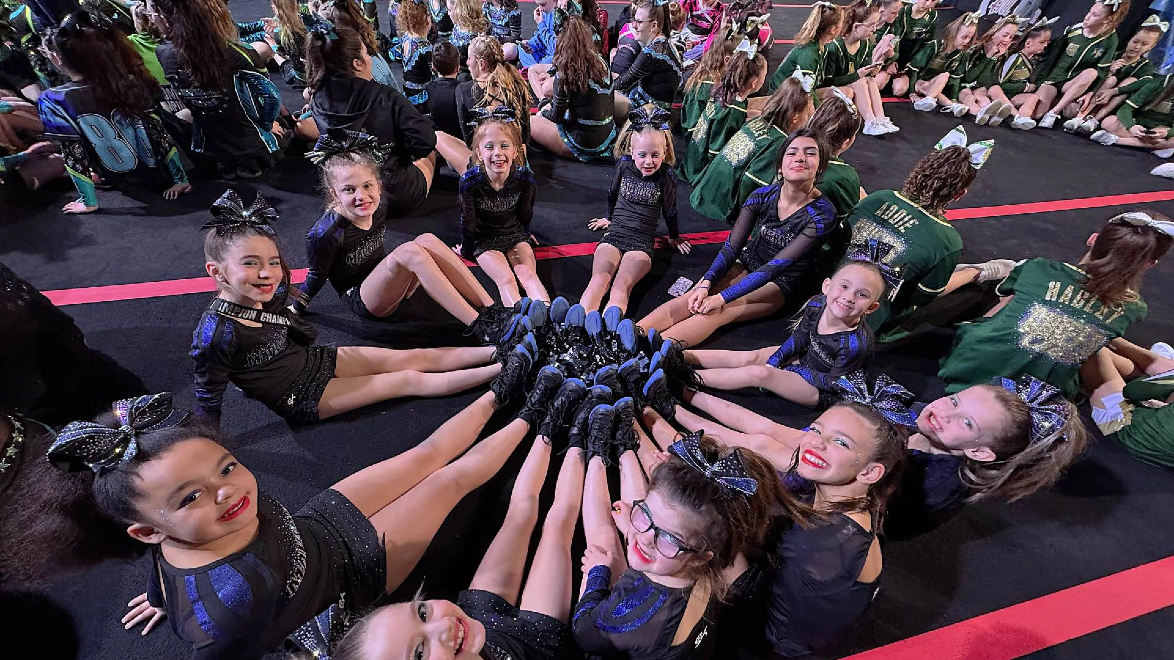 Group of 11 cheer leaders making a circle with legs in the middle smiling at the camera