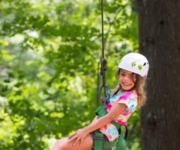 Girl with a giant smile and helmet hanging from a rope on the zip line
