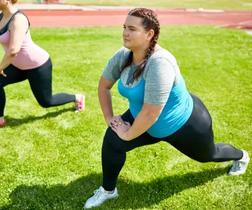 Group of friendly girls stretching legs in knee bend while exercising on green lawn