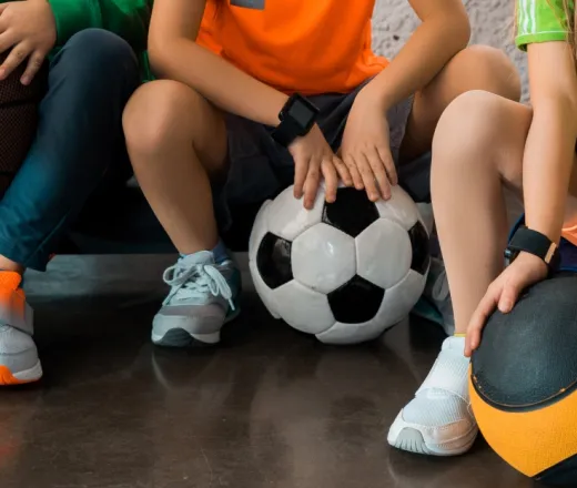 Cropped view of children sitting on step platforms with balls in gym, panoramic shot