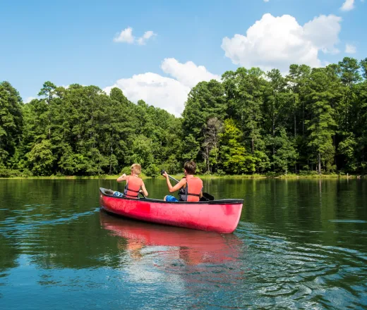 Two campers sitting in a red canoe out in the water surrounded by nature